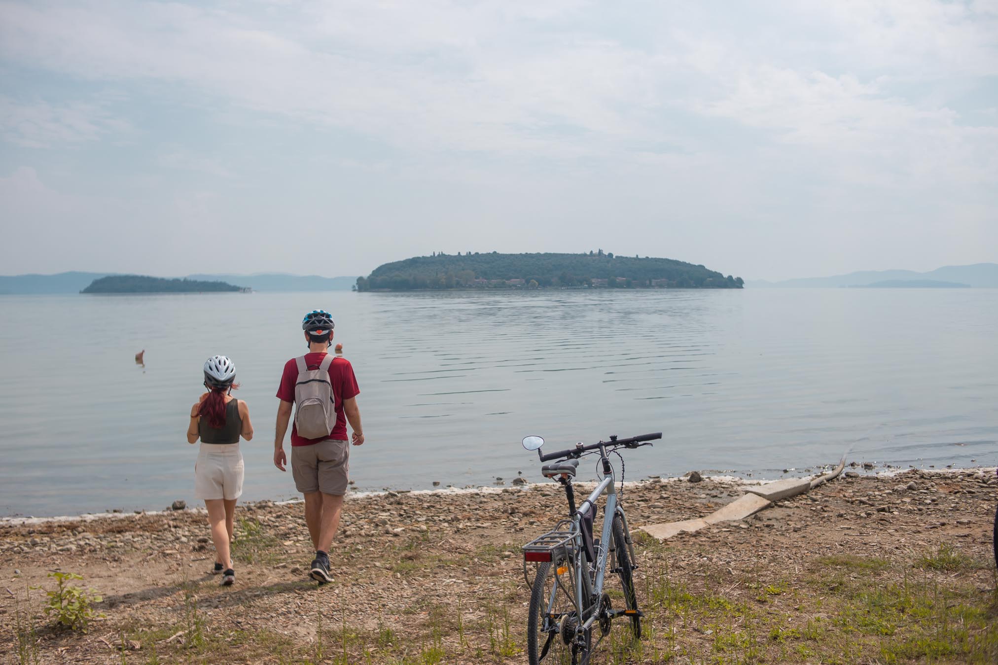 francesca e pietro camminano verso il lago trasimeno con la bicicletta a fianco